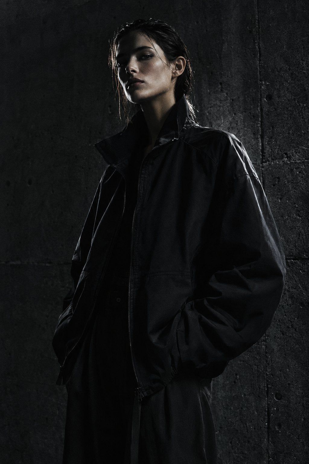 Model in black oversized jacket against concrete wall